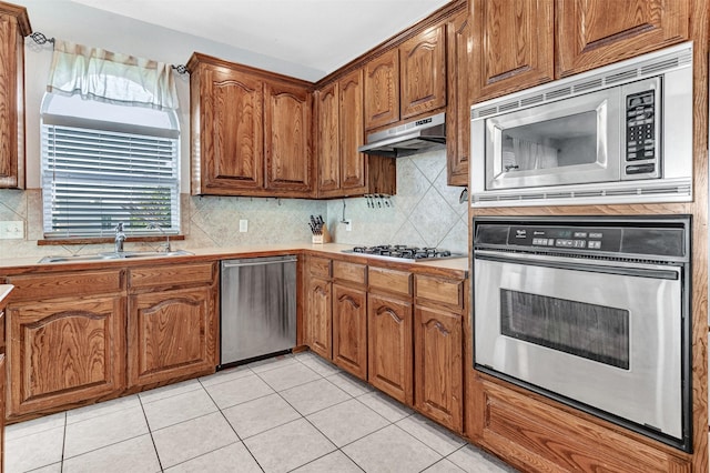 kitchen with appliances with stainless steel finishes, tasteful backsplash, light tile patterned floors, sink, and tile countertops