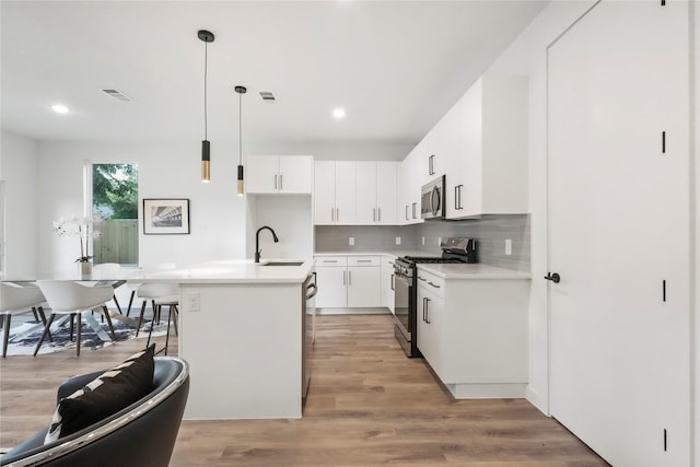 kitchen featuring a center island with sink, white cabinetry, hanging light fixtures, and appliances with stainless steel finishes