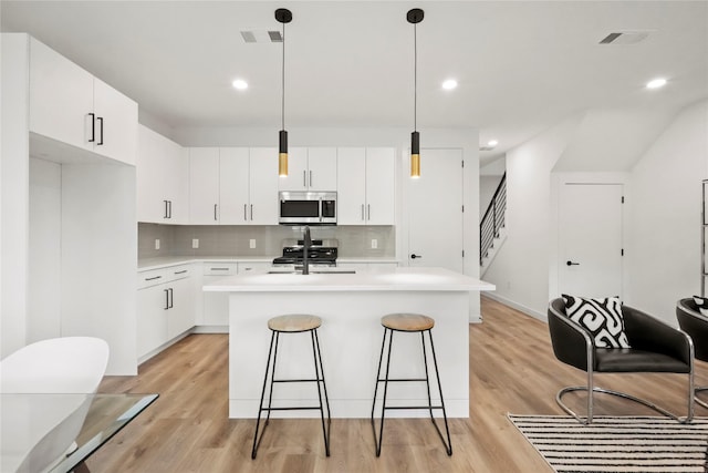 kitchen featuring pendant lighting, tasteful backsplash, a kitchen island with sink, white cabinetry, and appliances with stainless steel finishes