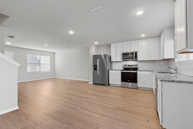 kitchen with stainless steel appliances, light stone counters, white cabinets, backsplash, and sink