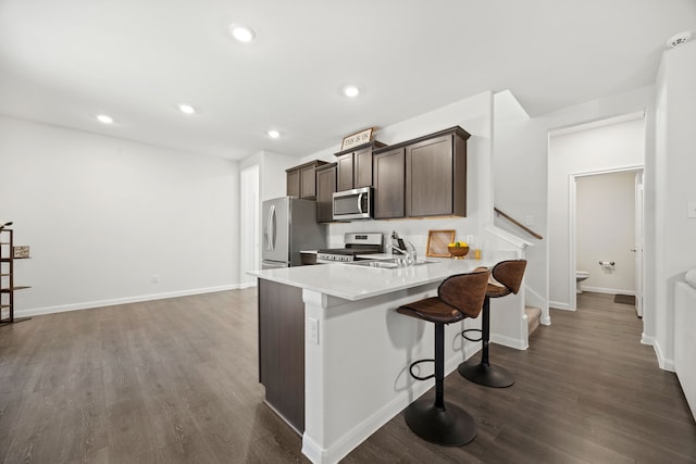 kitchen with stainless steel appliances, sink, dark brown cabinets, dark wood-type flooring, and a kitchen breakfast bar