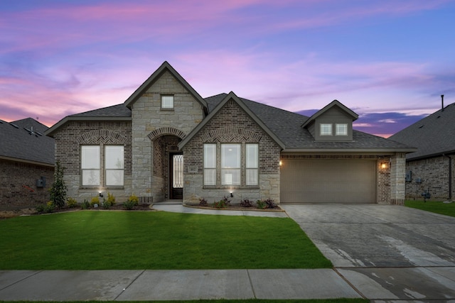 french country inspired facade featuring stone siding, concrete driveway, a yard, and an attached garage