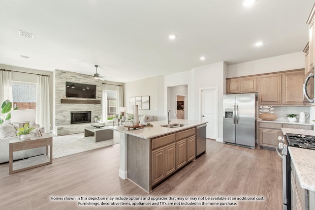 kitchen with sink, stainless steel appliances, a stone fireplace, and a center island with sink