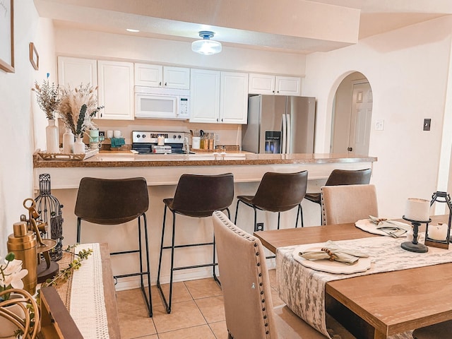 kitchen featuring stainless steel appliances, light tile patterned flooring, a breakfast bar, and white cabinetry