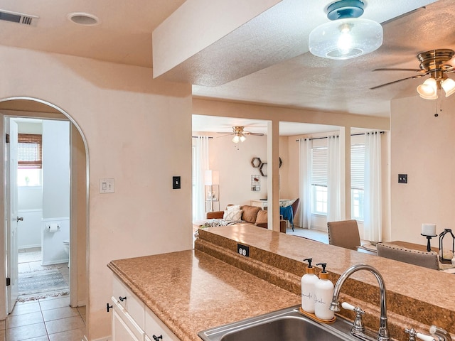 kitchen with sink, a textured ceiling, light tile patterned flooring, and white cabinetry