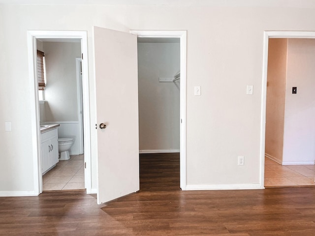 unfurnished bedroom with a walk in closet, ensuite bath, a closet, and dark wood-type flooring