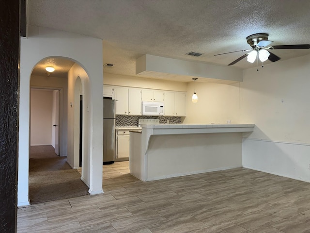 kitchen with decorative light fixtures, white cabinets, tile countertops, stainless steel refrigerator, and backsplash