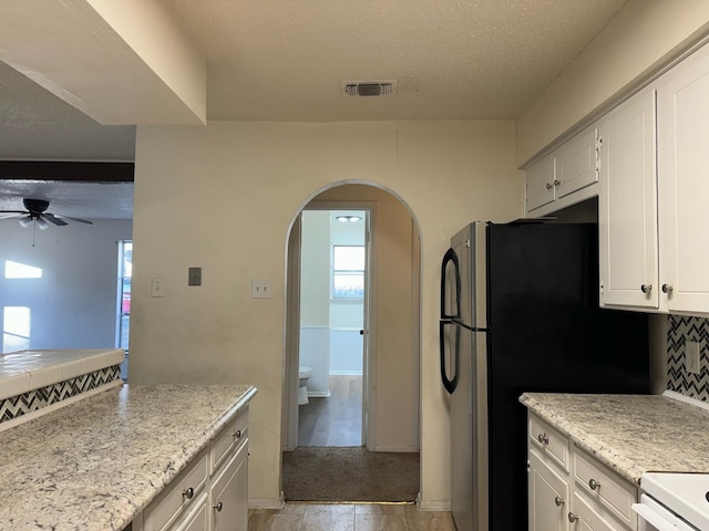 kitchen featuring stainless steel refrigerator, ceiling fan, decorative backsplash, a textured ceiling, and white cabinetry