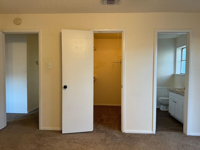 unfurnished bedroom with a closet, ensuite bath, dark colored carpet, a spacious closet, and a textured ceiling