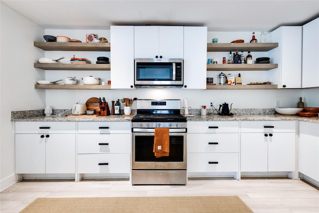 kitchen with white cabinetry, light stone counters, light hardwood / wood-style flooring, and appliances with stainless steel finishes