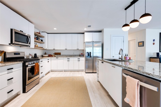 kitchen featuring white cabinets, stainless steel appliances, light hardwood / wood-style floors, and decorative light fixtures