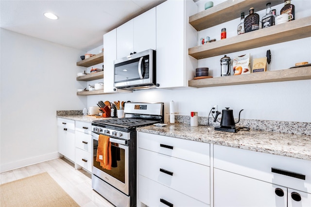 kitchen with stainless steel appliances, light wood-type flooring, light stone countertops, and white cabinets