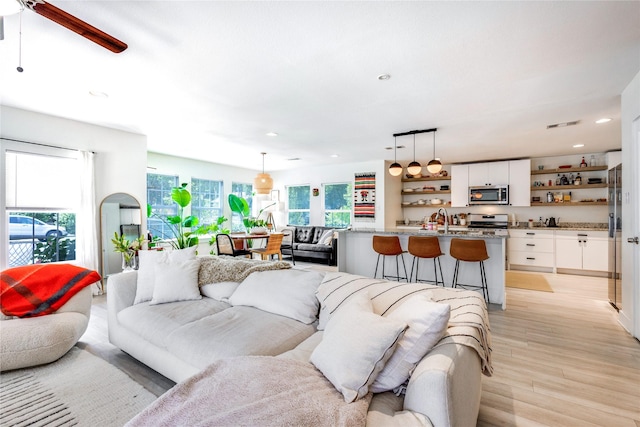 living room featuring ceiling fan, light hardwood / wood-style floors, sink, and plenty of natural light