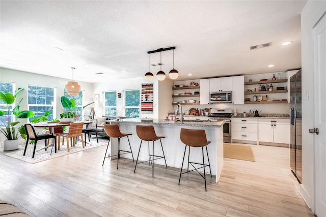 kitchen with decorative light fixtures, stainless steel appliances, light wood-type flooring, and white cabinetry