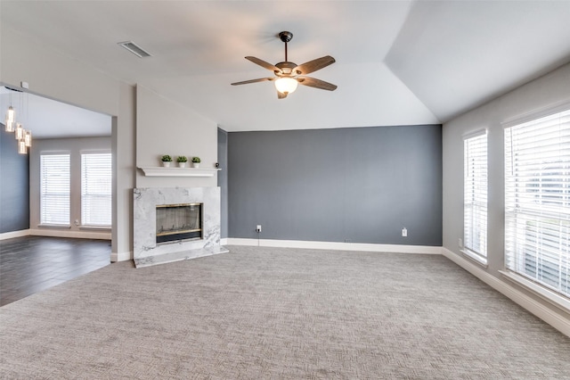 unfurnished living room with a high end fireplace, lofted ceiling, ceiling fan, and dark colored carpet