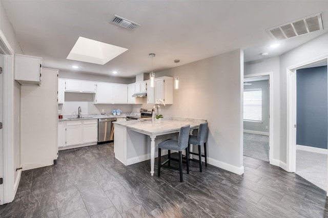 kitchen featuring stainless steel appliances, a skylight, white cabinets, decorative light fixtures, and sink