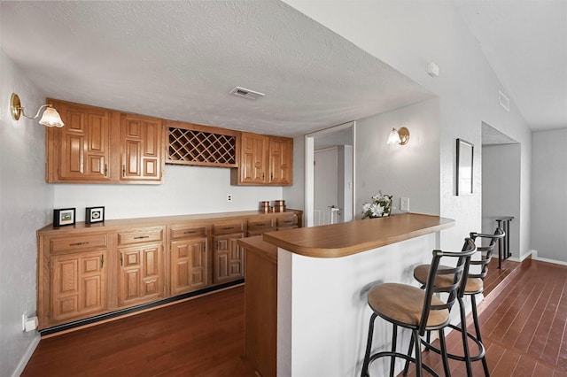 kitchen with dark wood-style floors, a textured ceiling, visible vents, and a breakfast bar area