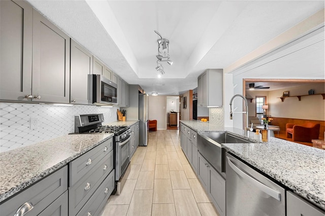 kitchen with tasteful backsplash, a tray ceiling, gray cabinets, stainless steel appliances, and a sink