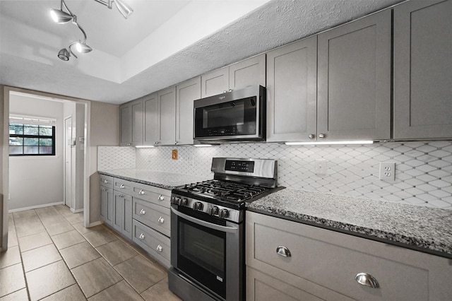 kitchen featuring gray cabinetry, baseboards, appliances with stainless steel finishes, decorative backsplash, and light stone countertops