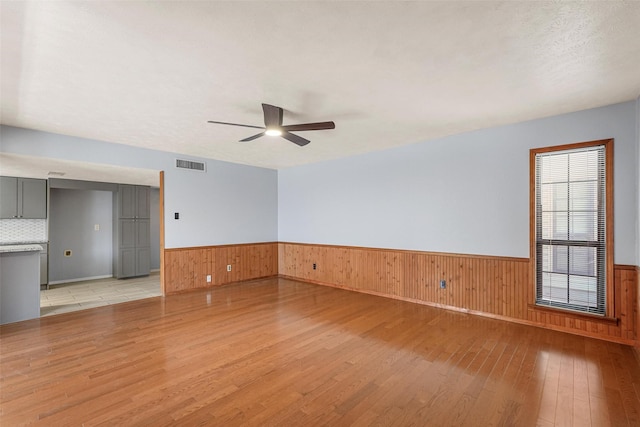 empty room featuring light wood finished floors, visible vents, a wainscoted wall, ceiling fan, and wood walls