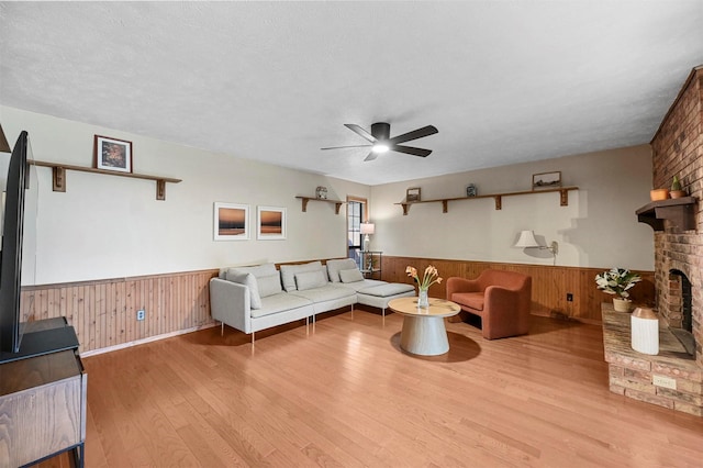 living room featuring ceiling fan, a brick fireplace, a textured ceiling, and light hardwood / wood-style floors