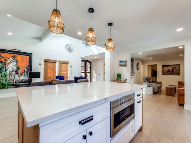 kitchen with vaulted ceiling, a center island, pendant lighting, stainless steel microwave, and white cabinetry