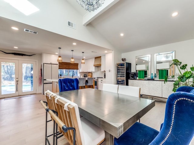 dining room with a chandelier, french doors, light wood-type flooring, vaulted ceiling with beams, and sink