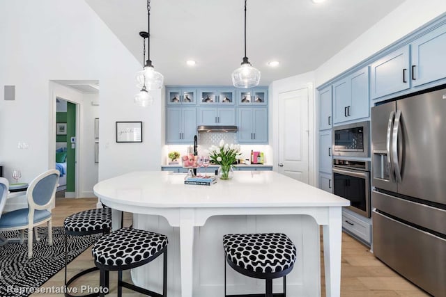 kitchen with hanging light fixtures, stainless steel appliances, a kitchen bar, backsplash, and blue cabinets