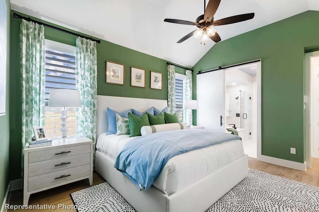 bedroom with vaulted ceiling, ensuite bathroom, hardwood / wood-style floors, a barn door, and ceiling fan