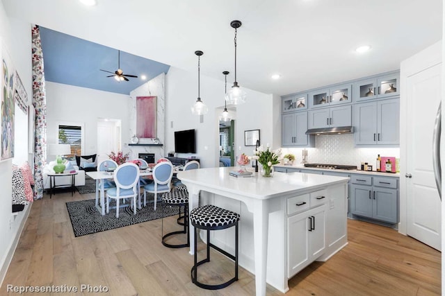 kitchen featuring a kitchen island with sink, light wood-type flooring, ceiling fan, decorative light fixtures, and tasteful backsplash