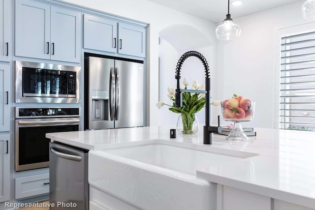 kitchen featuring light stone countertops, built in microwave, stainless steel fridge, pendant lighting, and sink