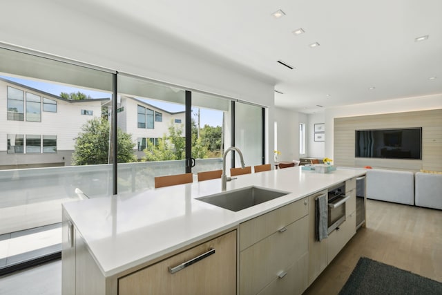 kitchen with a large island with sink, light hardwood / wood-style flooring, light brown cabinets, and sink