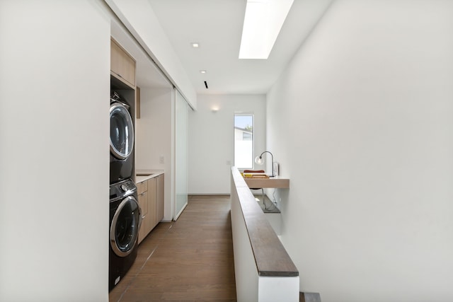 laundry room with stacked washer and dryer, cabinets, a skylight, dark hardwood / wood-style flooring, and sink