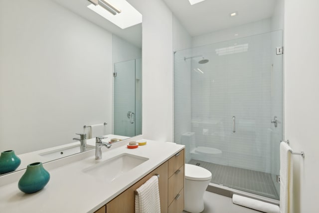 bathroom with toilet, a skylight, a shower with shower door, and vanity