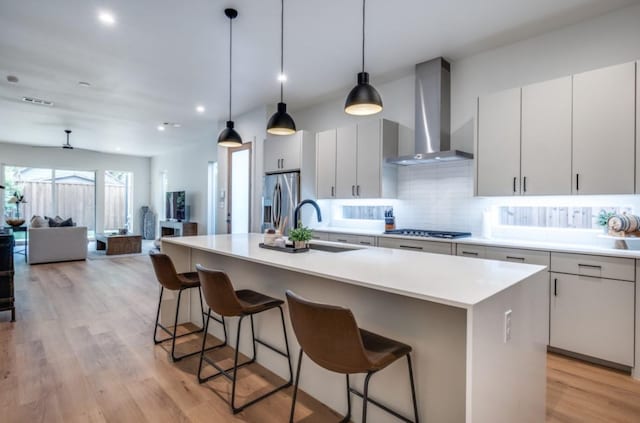 kitchen featuring sink, wall chimney range hood, appliances with stainless steel finishes, and a center island with sink