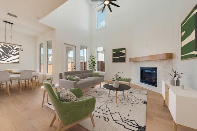 unfurnished living room featuring ceiling fan, light hardwood / wood-style floors, a towering ceiling, and a fireplace