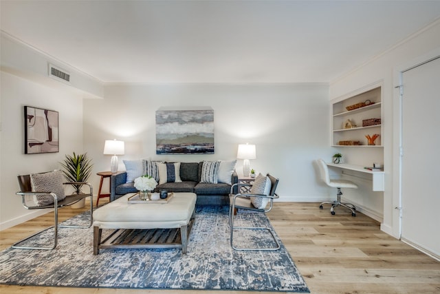 living room with built in desk, light wood-type flooring, built in features, and ornamental molding