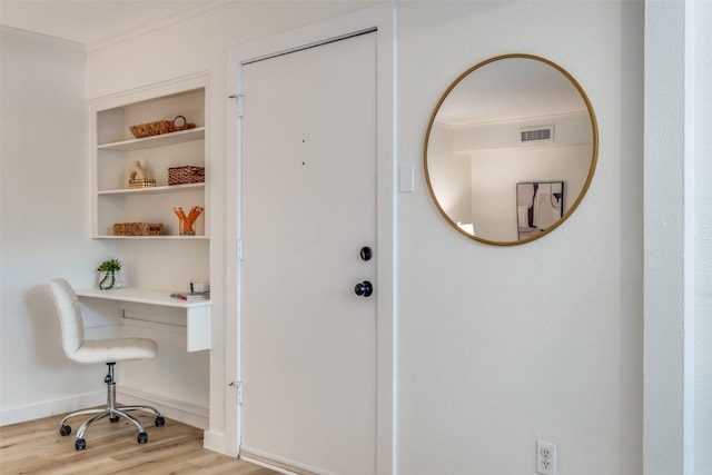 office with light wood-type flooring, built in features, and ornamental molding