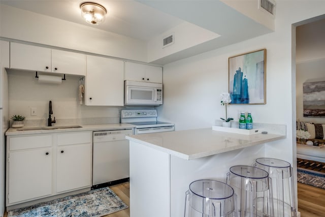 kitchen featuring white appliances, light hardwood / wood-style floors, white cabinets, a kitchen breakfast bar, and sink