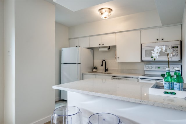 kitchen featuring sink, white cabinets, white appliances, a breakfast bar area, and light stone countertops