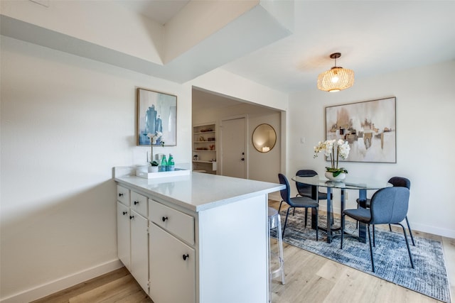 kitchen featuring kitchen peninsula, light hardwood / wood-style flooring, hanging light fixtures, and white cabinetry