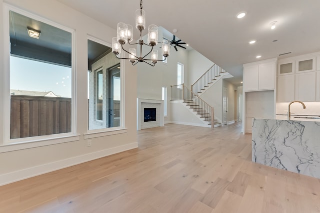 unfurnished living room with sink, ceiling fan with notable chandelier, and light hardwood / wood-style flooring