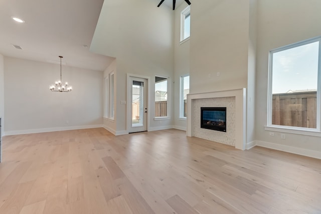 unfurnished living room featuring light wood-type flooring, an inviting chandelier, and a towering ceiling