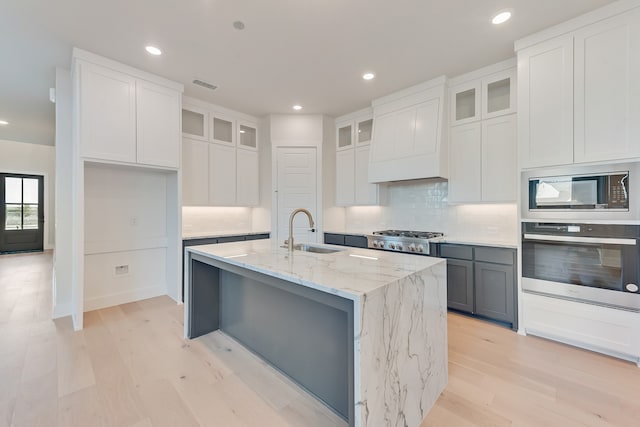 kitchen featuring stainless steel appliances, sink, white cabinetry, an island with sink, and light stone countertops