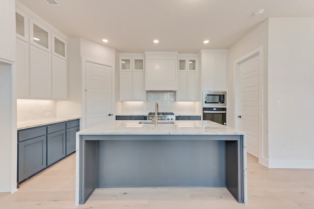 kitchen with white cabinetry, stainless steel microwave, light wood-type flooring, and an island with sink