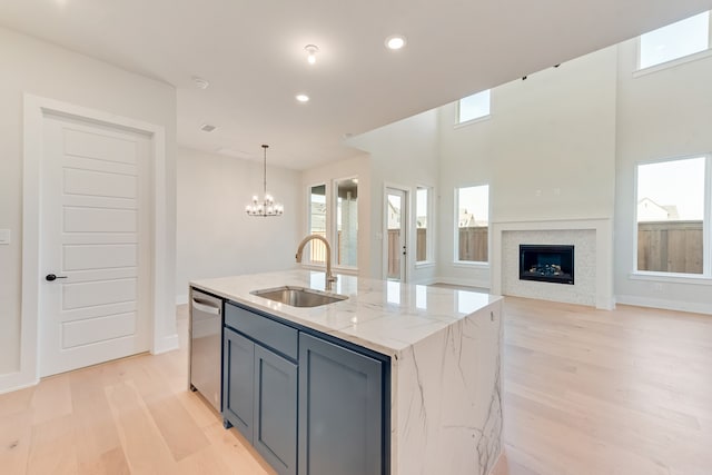 kitchen with dishwasher, a center island with sink, light wood-type flooring, light stone counters, and sink