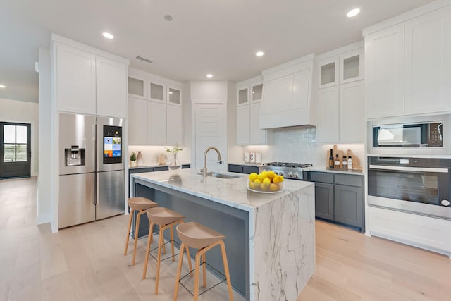 kitchen with sink, white cabinets, light stone countertops, a kitchen island with sink, and appliances with stainless steel finishes