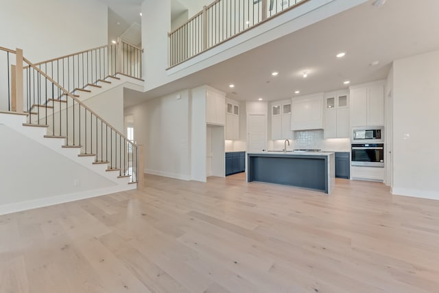 kitchen with an island with sink, stainless steel oven, built in microwave, white cabinets, and light hardwood / wood-style flooring