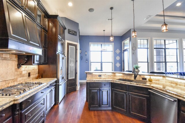 kitchen featuring hanging light fixtures, stainless steel appliances, backsplash, ventilation hood, and sink