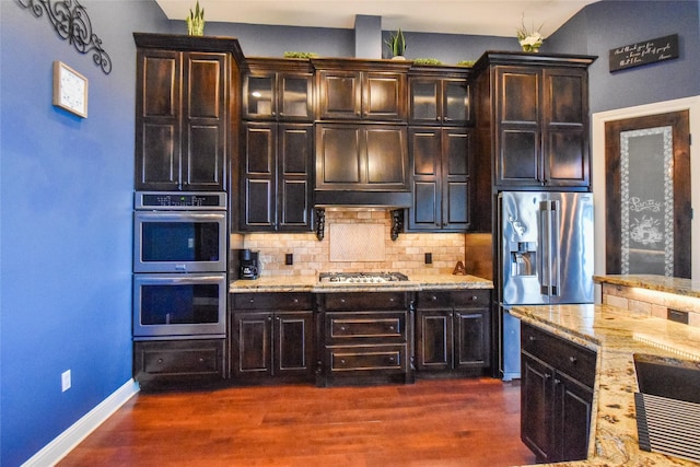 kitchen with appliances with stainless steel finishes, dark hardwood / wood-style floors, light stone counters, and tasteful backsplash